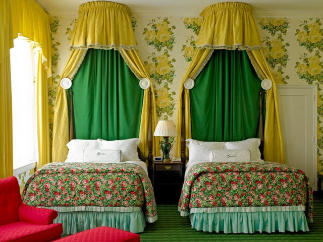 Bedroom with two beds, yellow canopy drapes, green curtains, floral comforters, and floral