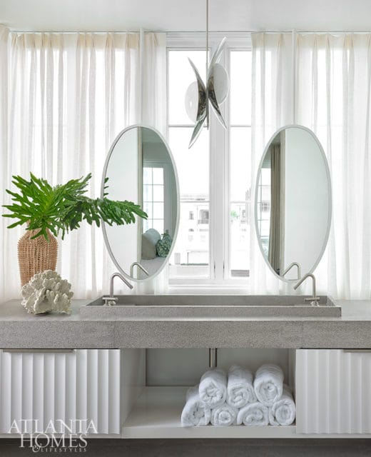 Modern bathroom with double oval mirrors, concrete vanity, and fluted white cabinets.