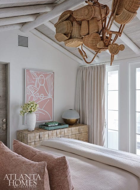 Bedroom with pink abstract art, rattan chandelier, and wood dresser
