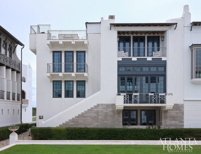 White modern house with dark windows, balconies, and stairs. Atlanta Homes & Lifestyles logo.
