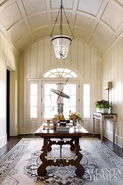 Foyer with paneled ceiling, arched doorway, console table with decorative objects, and ornate rug.