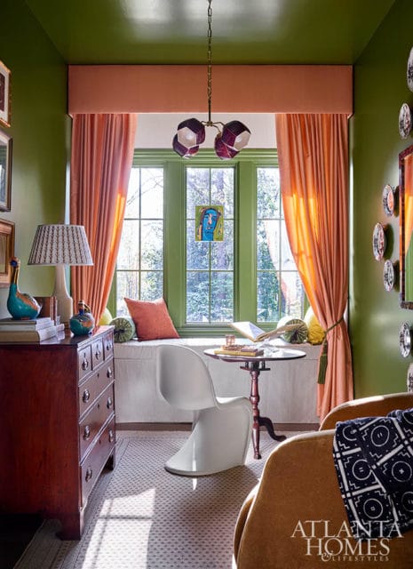 Green room with peach curtains, bay window, white chair, and wooden dresser.