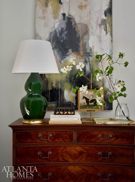 Green gourd lamp on mahogany dresser with abstract art and dogwood branches