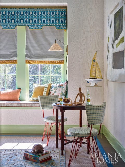 Window seat with patterned pillows, plaid chairs at a round table, and artwork on wood-grain