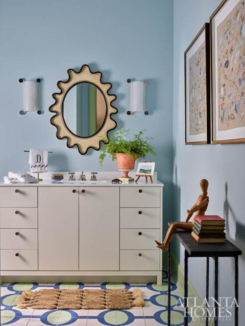 Light blue bathroom with cream vanity, sunburst mirror, and graphic floor tiles.