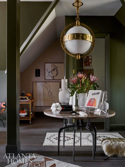Marble round table with abstract sculpture, books, and protea flowers. Green walls.