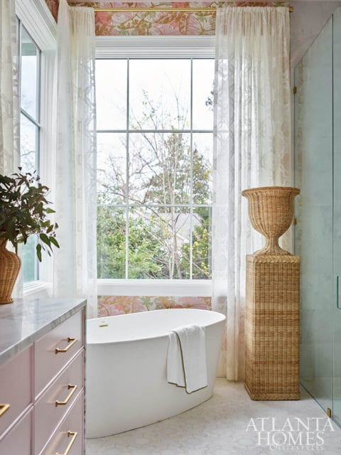 Freestanding white bathtub with a towel, pink vanity, and floral wallpaper.