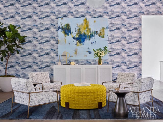 Living room with blue cloud wallpaper, four chairs, yellow ottoman, and abstract art.