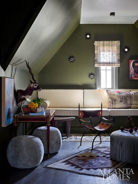Olive green room with built-in bench, leather chair, taxidermy antelope, and patterned rug.