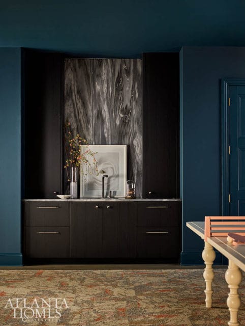 Dark wood cabinetry with marble backsplash, framed art, and sink. Blue walls and patterned rug.