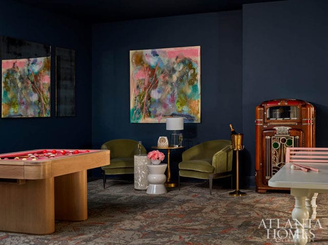 Dark blue room with pool table, two green chairs, abstract art, and vintage jukebox.