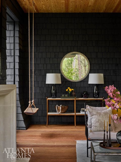 Black shingle wall interior with wooden swing, console table, and seating area.