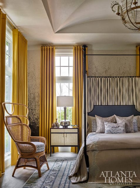 Bedroom with yellow curtains, rattan chair, four-poster bed, and Atlanta Homes & Lifestyles logo