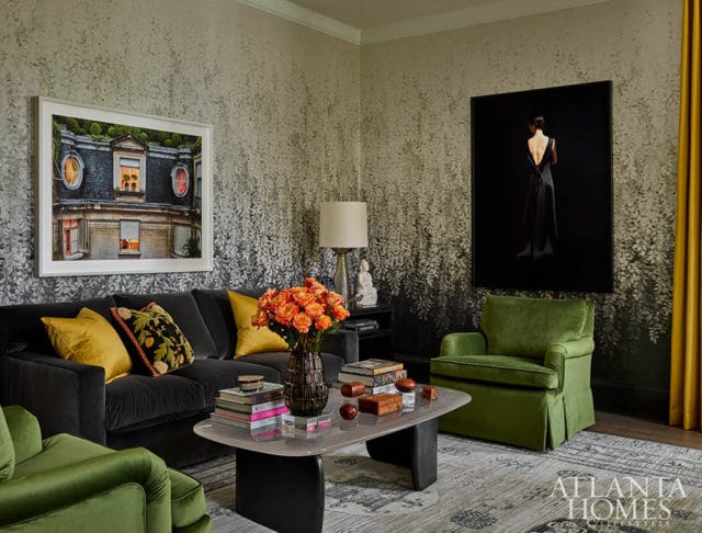 Living room with dark gray sofa, green armchairs, floral wallpaper, and artwork.