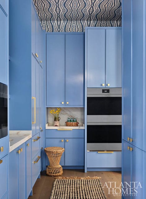 Blue kitchen with marble countertops, gold hardware, and a patterned ceiling.