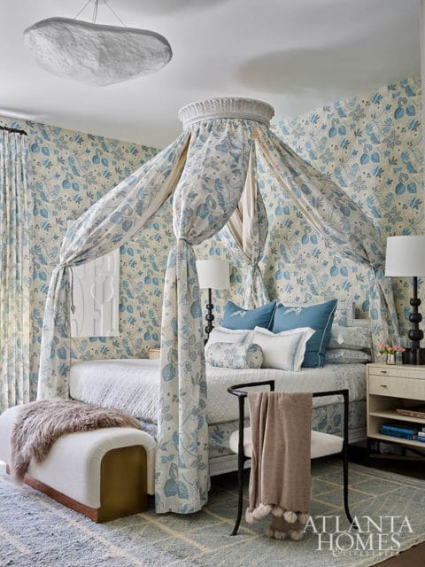 Bedroom with blue floral wallpaper, canopy bed with blue floral drapes, and white bench with fur