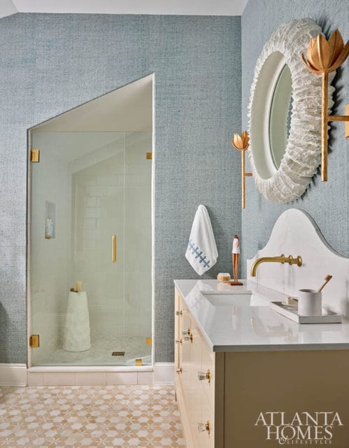 Blue textured wallpaper bathroom with glass shower, vanity, and ornate mirror.