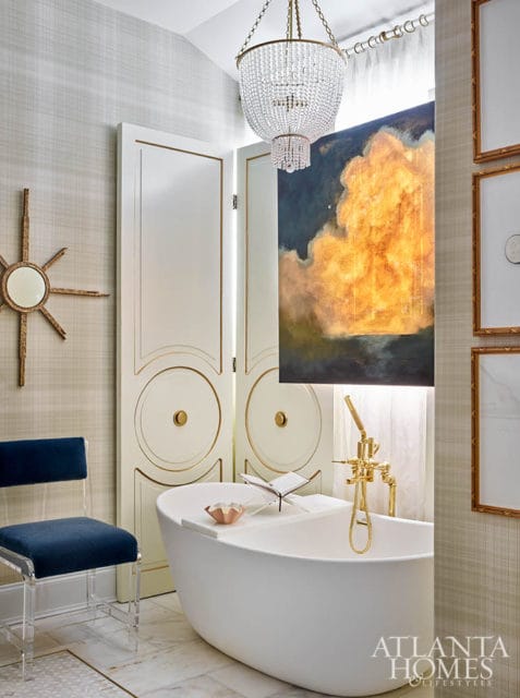 White bathtub with gold faucet, abstract painting, and crystal chandelier.