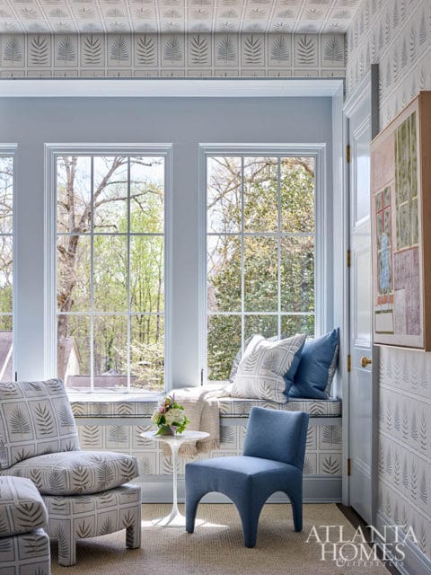 Light blue room with patterned wallpaper, window seat, two chairs, and a small side table.