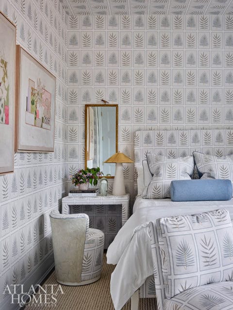 Bedroom with palm leaf patterned wallpaper, upholstered headboard, and matching accent chairs.