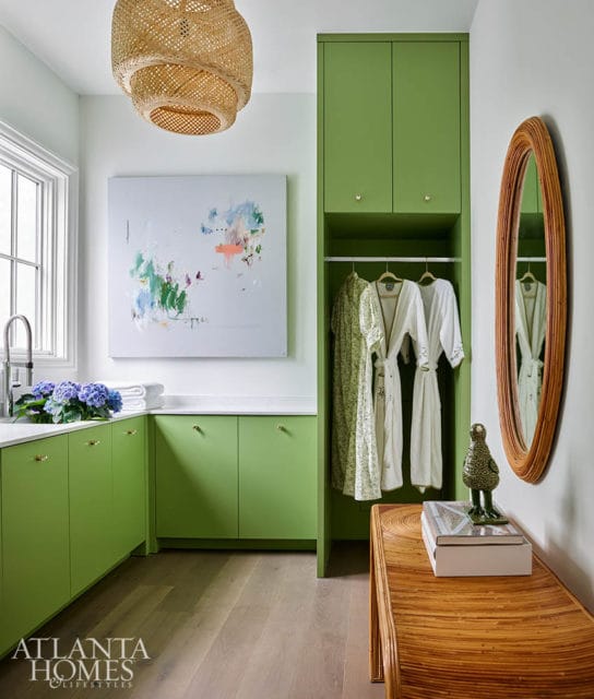 Green cabinets and closet with robes, abstract art, and rattan mirror