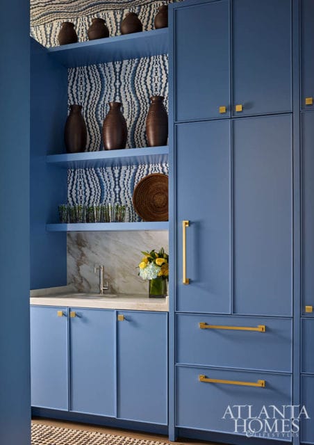 Blue kitchen cabinets with brass hardware, marble countertop, and patterned wallpaper.