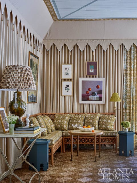 Rattan sectional sofa with floral cushions, draped curtains, and artwork in a living room.