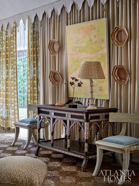 Ornate wooden console table with inlaid details, flanked by chairs, under abstract art.