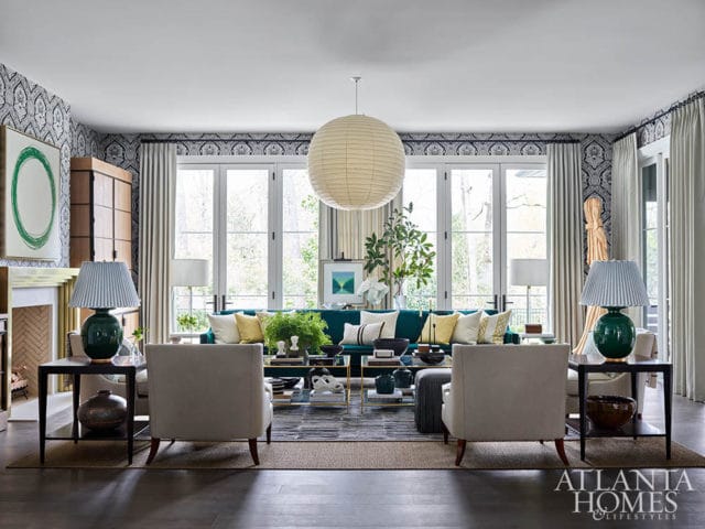 Living room with teal sofa, cream armchairs, patterned wallpaper, and large paper lantern light.