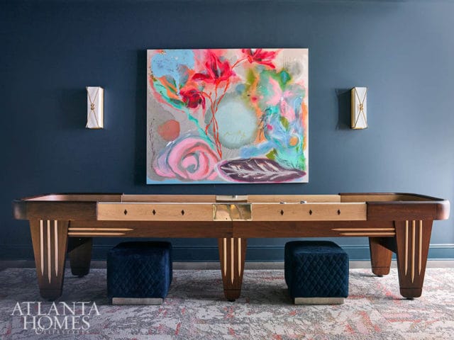 Dark blue room with abstract art above a wooden pool table and two navy ottomans.