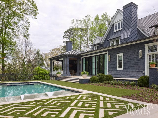 Dark blue shingle-clad house with pool, covered patio, and geometric lawn design.