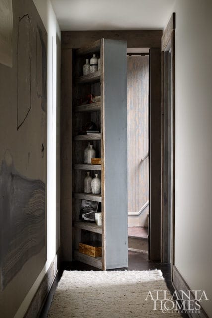 Hallway with open shelving unit displaying bottles and boxes, leading to stairs.
