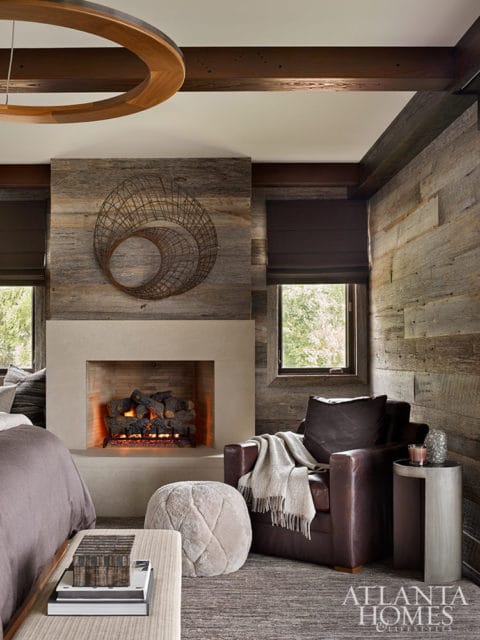 Bedroom with stone fireplace, leather armchair, and wood-paneled walls. Atlanta Homes logo.