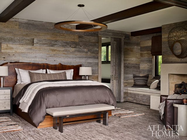 Bedroom with wood plank walls, live-edge headboard, circular pendant light, and stone fireplace.