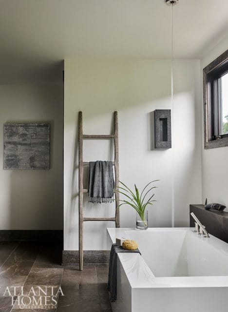 Modern white bathtub with a wooden ladder holding a gray towel.