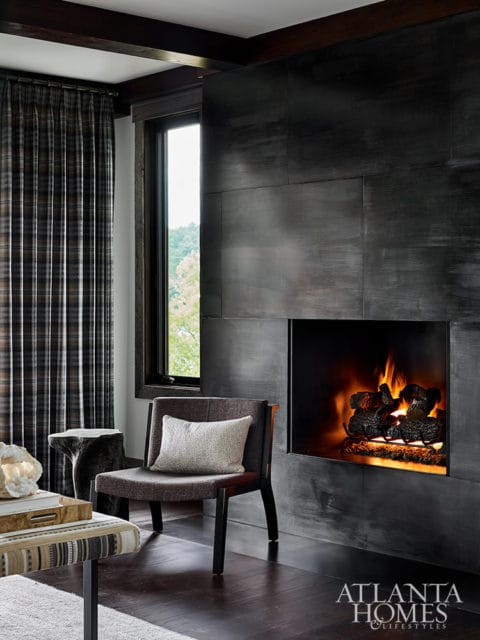 Living room with a dark tiled fireplace, plaid curtains, and a modern armchair with a pillow.