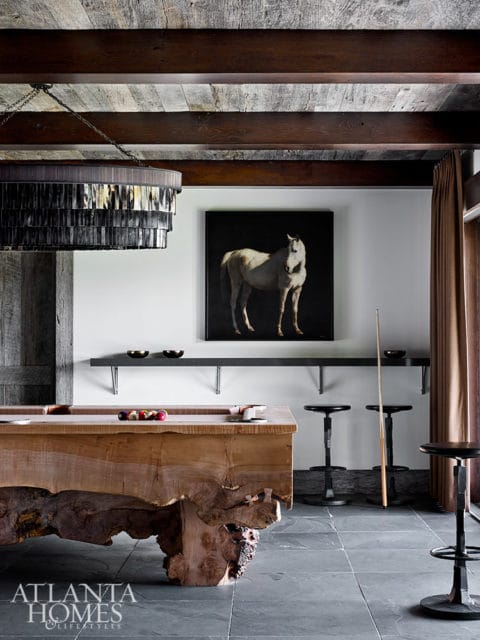Rustic game room with live-edge pool table, horse painting, and dark metal stools.