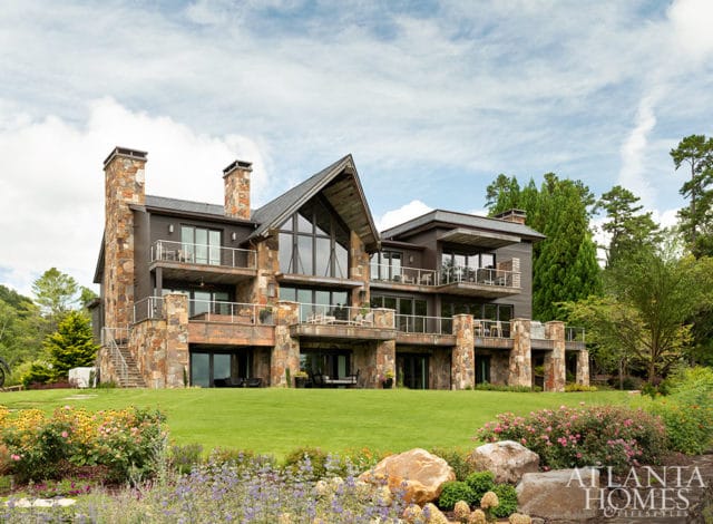 Modern home with stone accents, multiple balconies, and large windows overlooking a lawn and garden.
