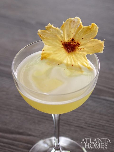 Yellow cocktail garnished with a dried pineapple flower and sprinkled with red spice