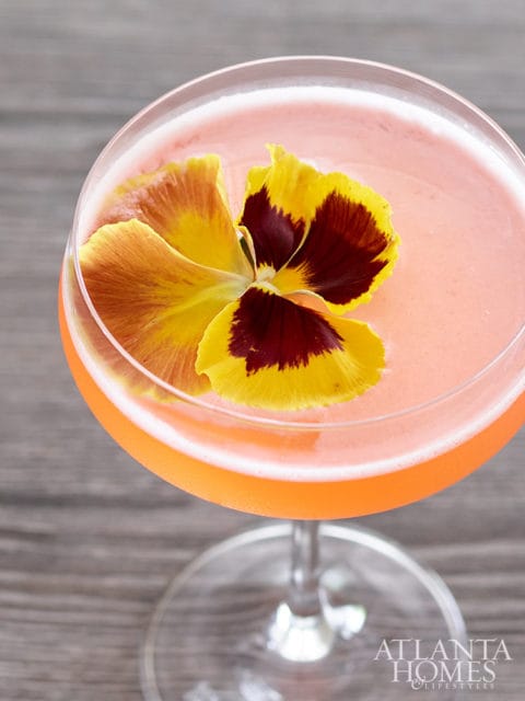 Pink cocktail in a coupe glass garnished with a yellow and burgundy pansy