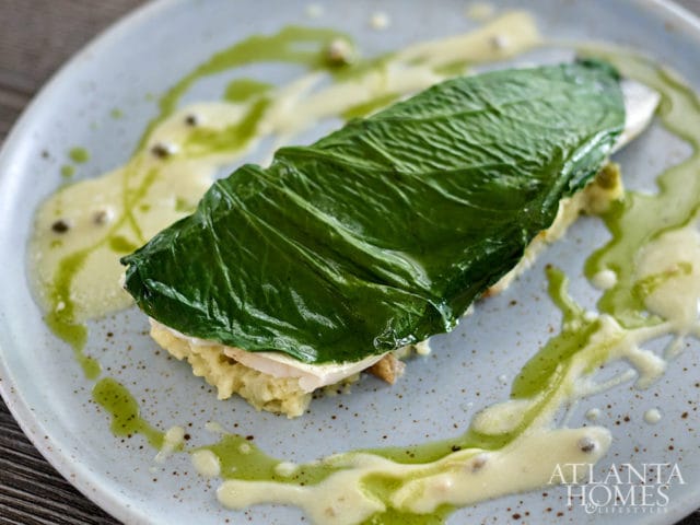 Fish fillet topped with a large green leaf on a bed of mashed vegetables, drizzled with sauce.