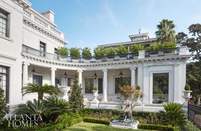 White brick mansion with curved portico, columns, and rooftop garden.