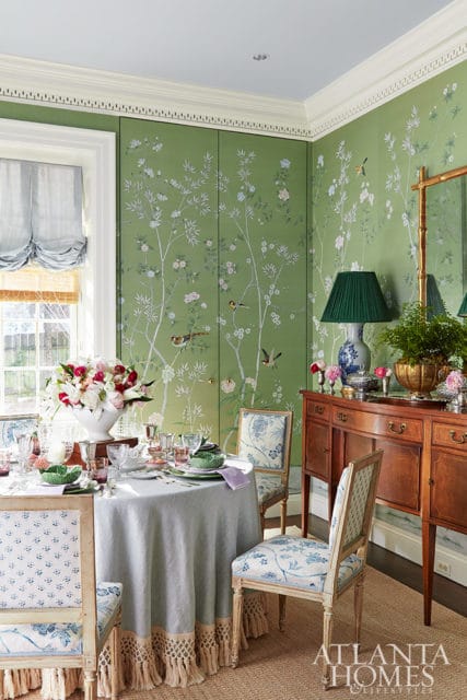 Dining room with green floral wallpaper, round table set for dinner, and wooden buffet.