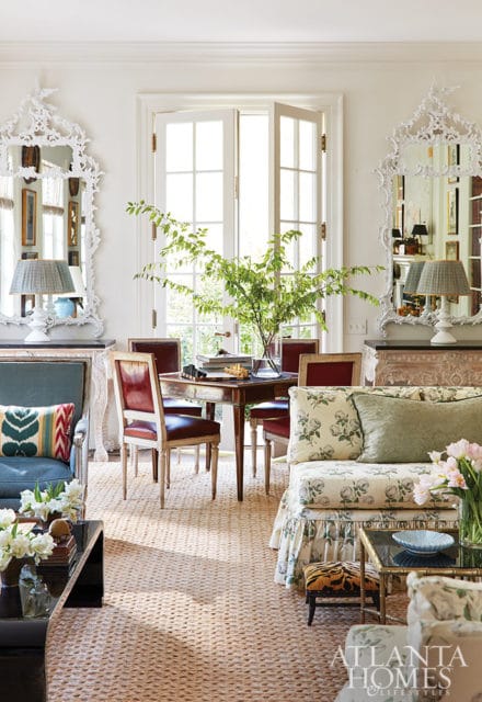Living room with white ornate mirrors, red leather chairs around a table, and floral patterned sofa.
