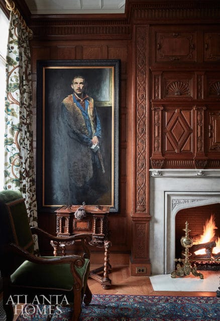 Study with wood paneling, fireplace, portrait of a man, and green velvet chair.