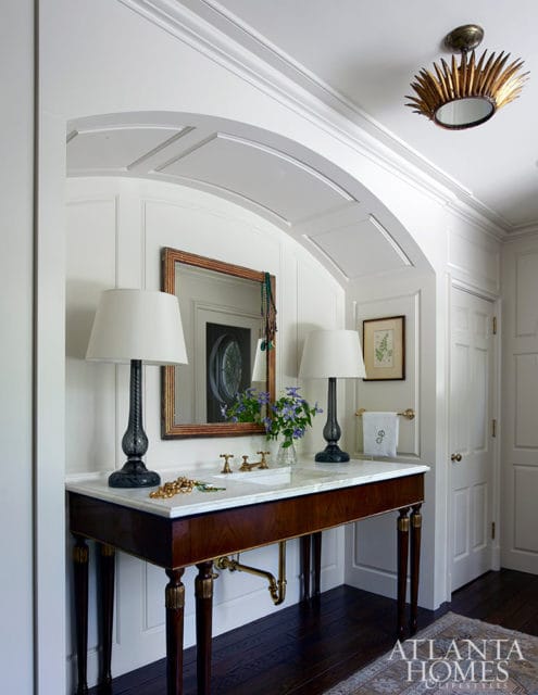 White dressing room with marble vanity, dark wood legs, and brass fixtures.