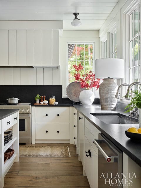 White kitchen with black countertops, stainless steel appliances, and a window view of trees
