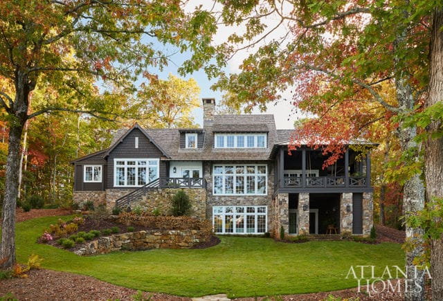 Stone and dark wood house with multiple windows and a screened porch, surrounded by fall foliage.