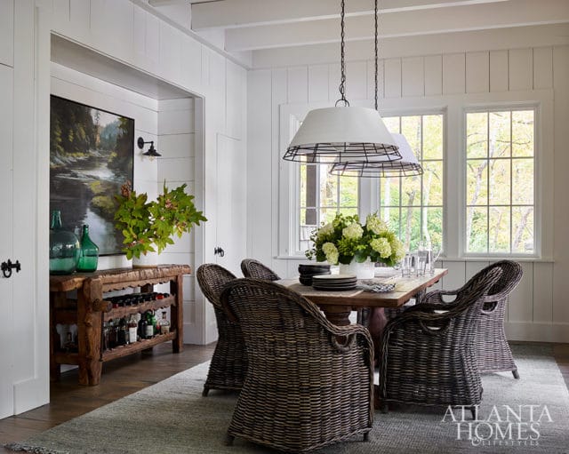 Dining room with wicker chairs, wooden table, and pendant lights. Painting on wall.
