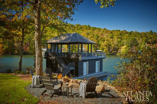 Dark wood boathouse with upper deck and Adirondack chairs on gravel patio by lake